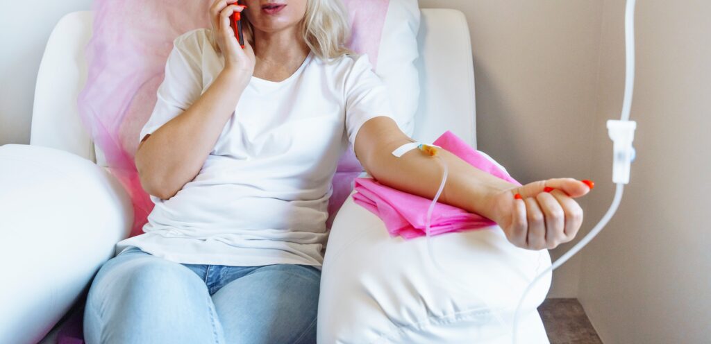 A woman receiving IV therapy at home while talking on the phone, seated in a comfortable chair with a relaxed ambiance.