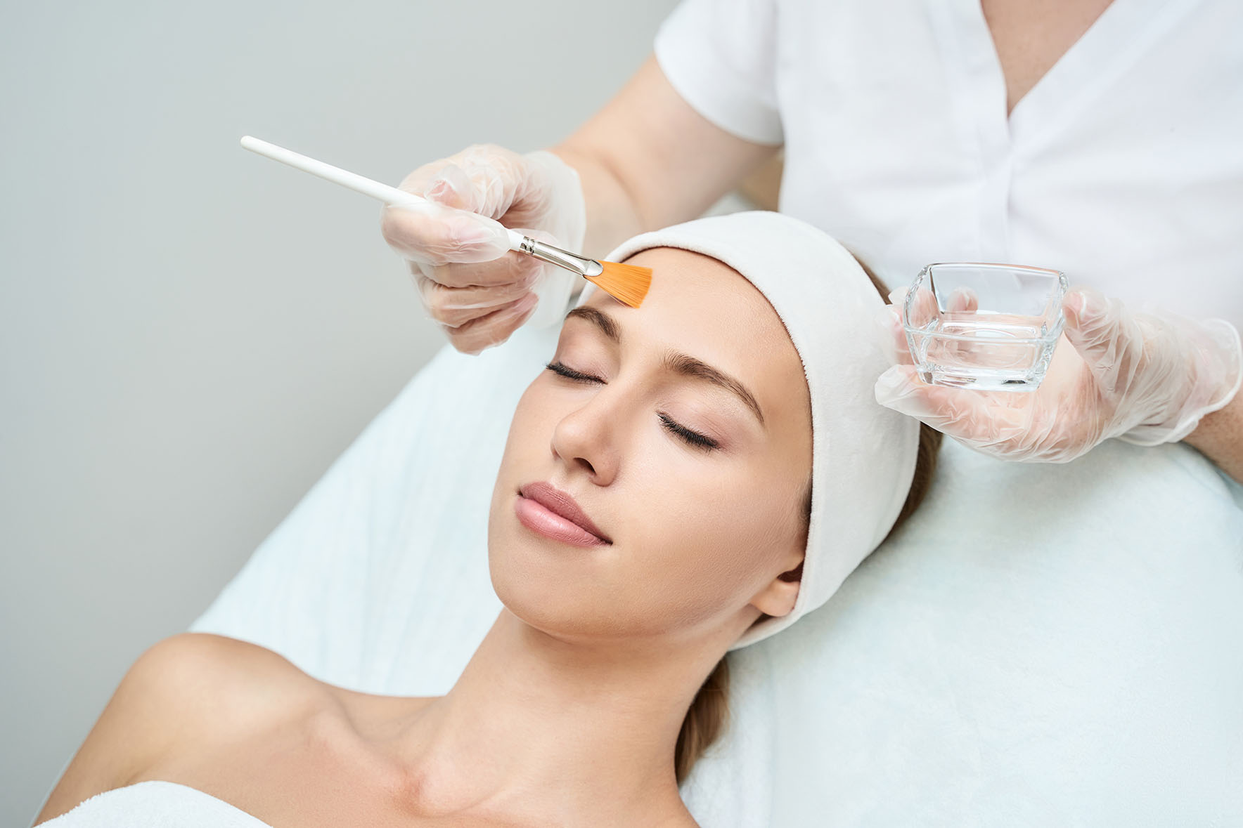Practitioner applying liquid to a woman's forehead with a brush as she lies with eyes closed.