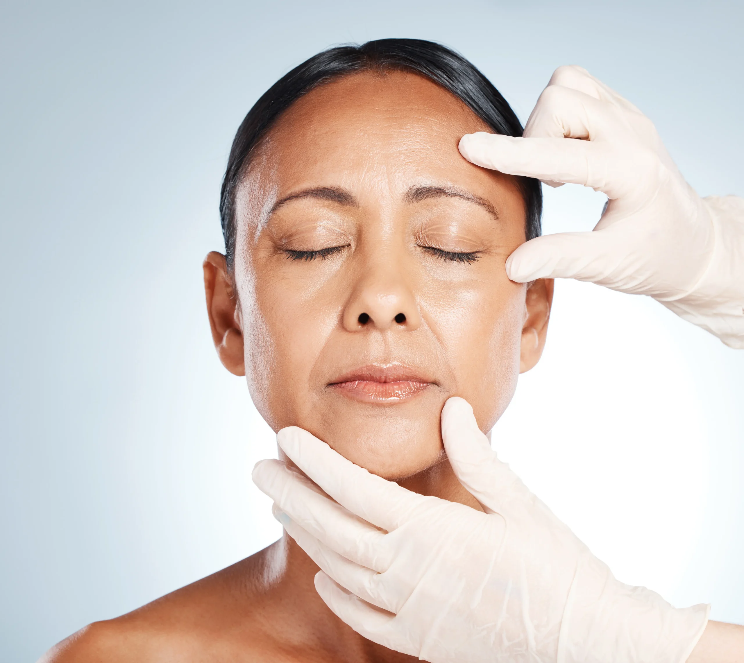 Gloved hands gently assessing woman’s face during skin treatment